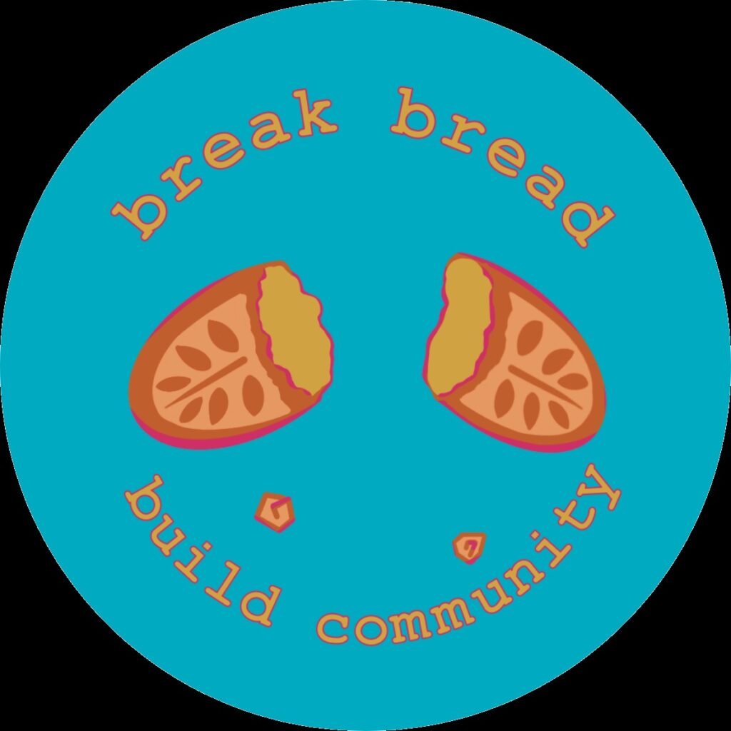 Sticker says "Break Bread, Build Community" around a broken loaf of bread with a leaf design etched into the dough. Bright blue background with gold and golden brown hues for the loaf, a mild pink outline of the text and illustration. Small crumbs bounce down toward "build community."